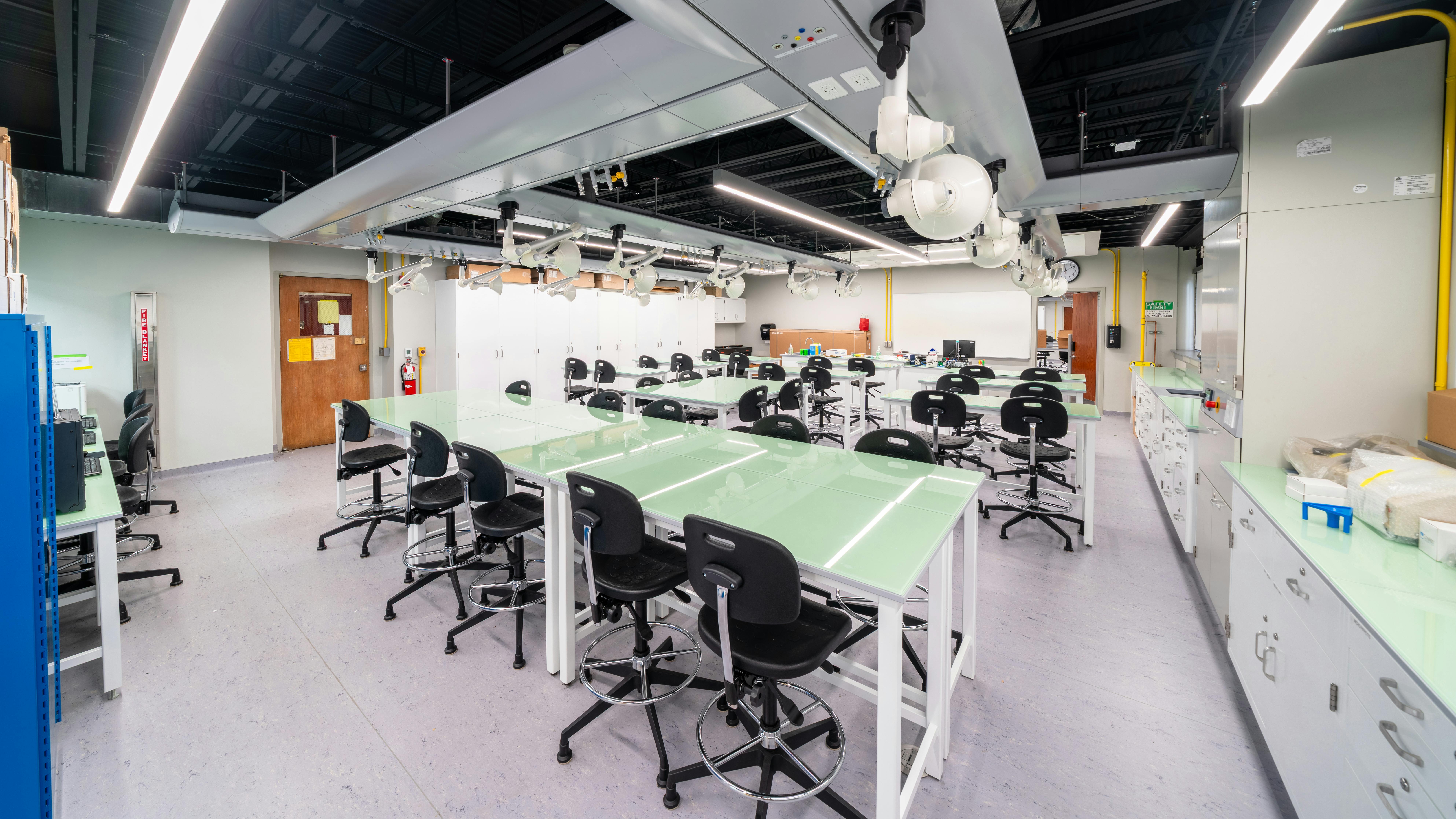Modern science classroom with glass-top tables and stool-height chairs.