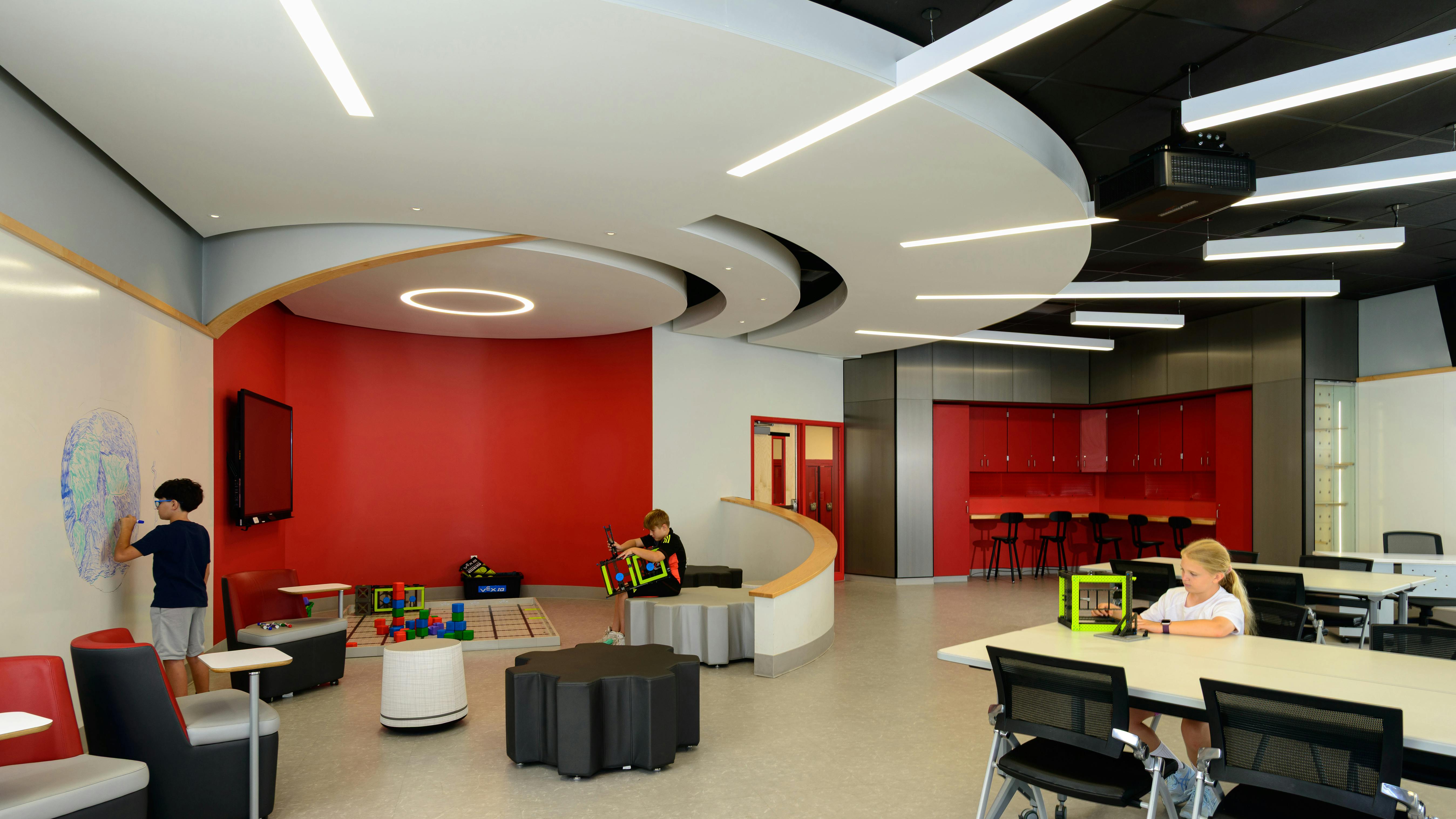 Modern classroom with variety of seating areas, writable walls, and oculus-shaped ceiling with lighting fixtures extending outward.