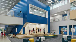 Large two-story atrium space with casual seating and a stage area with kids exercising with teacher.