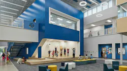 Large two-story atrium space with casual seating and a stage area with kids exercising with teacher.
