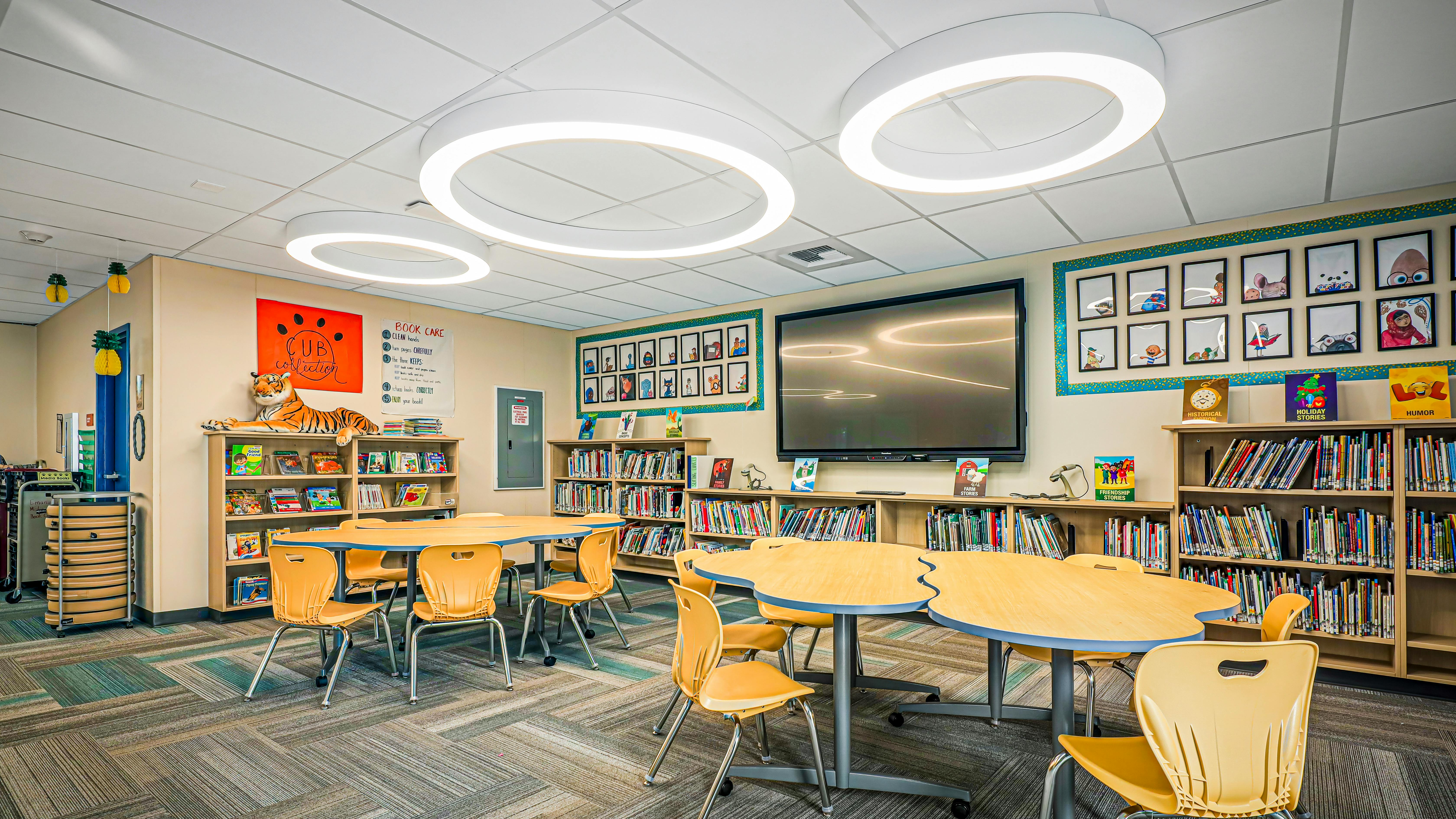 Media center with tables, chairs, bookshelves, and circular lighting fixtures in the ceiling.