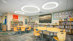 Media center with tables, chairs, bookshelves, and circular lighting fixtures in the ceiling.