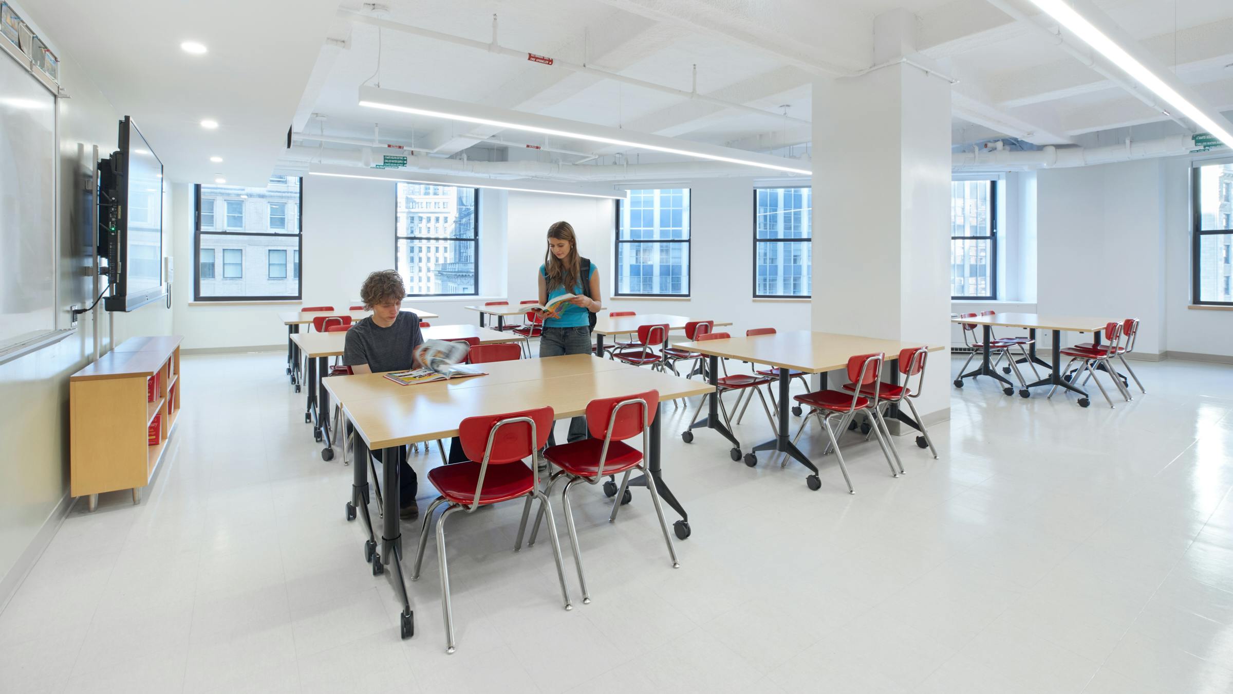 Students sit in a brighly-lit classroom with modern tables and chairs.