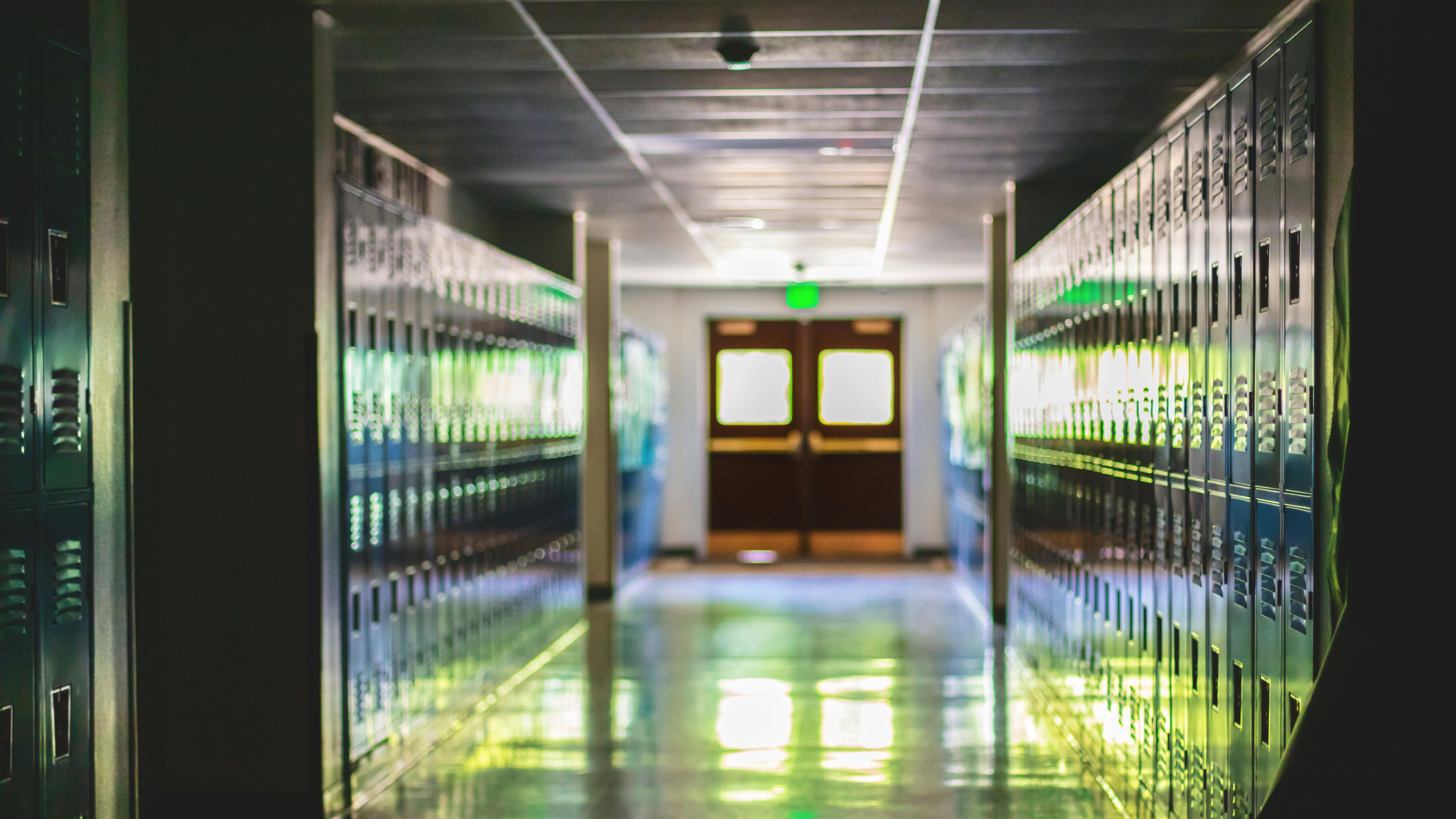 Distant double entry doors in empty school hallway lined with lockers