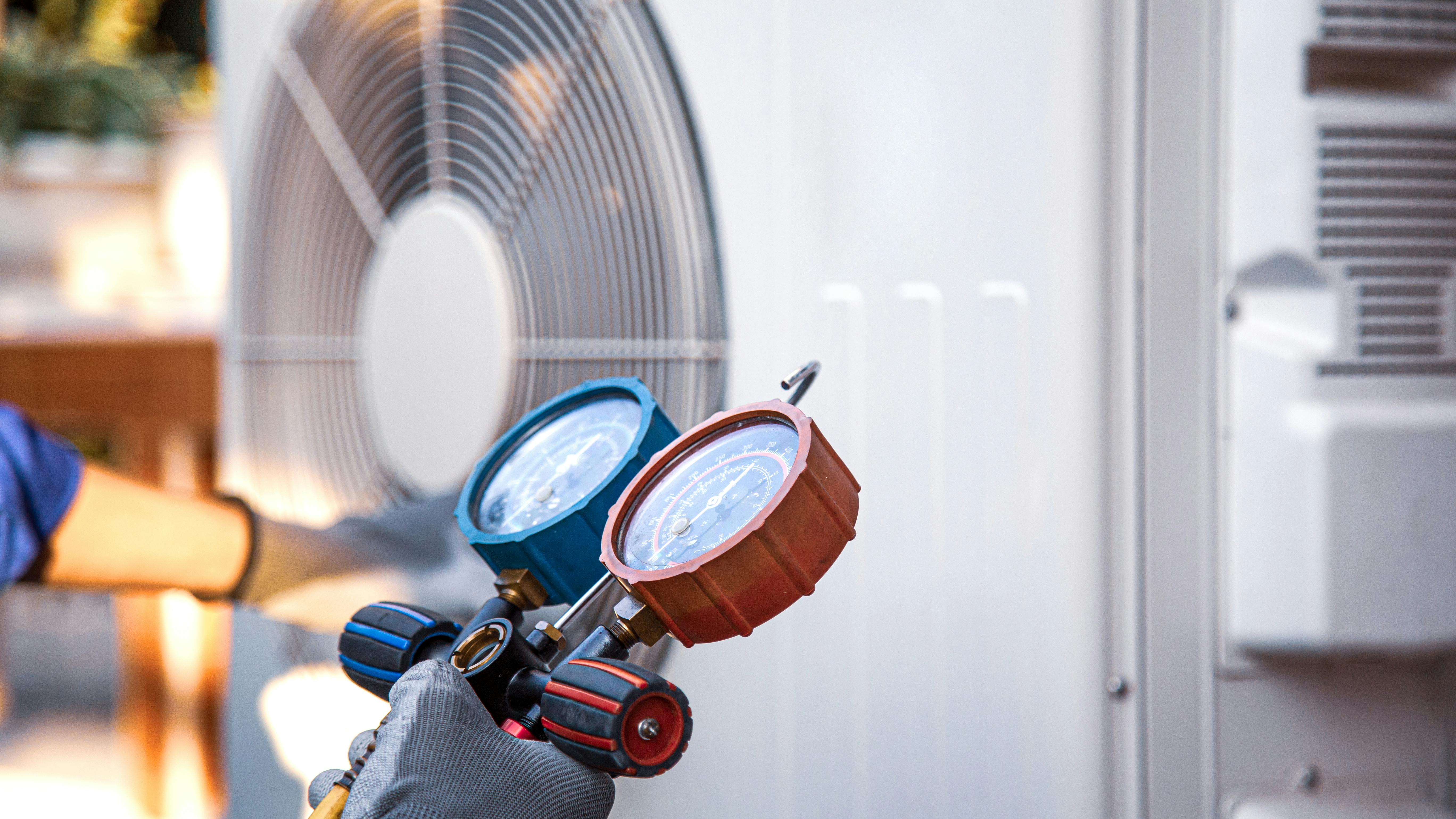 Heat and Air Conditioning, HVAC system service technician using measuring manifold gauge checking refrigerant and filling industrial air conditioner after duct cleaning maintenance outdoor compressor.
