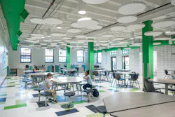 Bright, modern cafeteria space in elementary school with colorful accents and circular acoustic ceiling baffles.