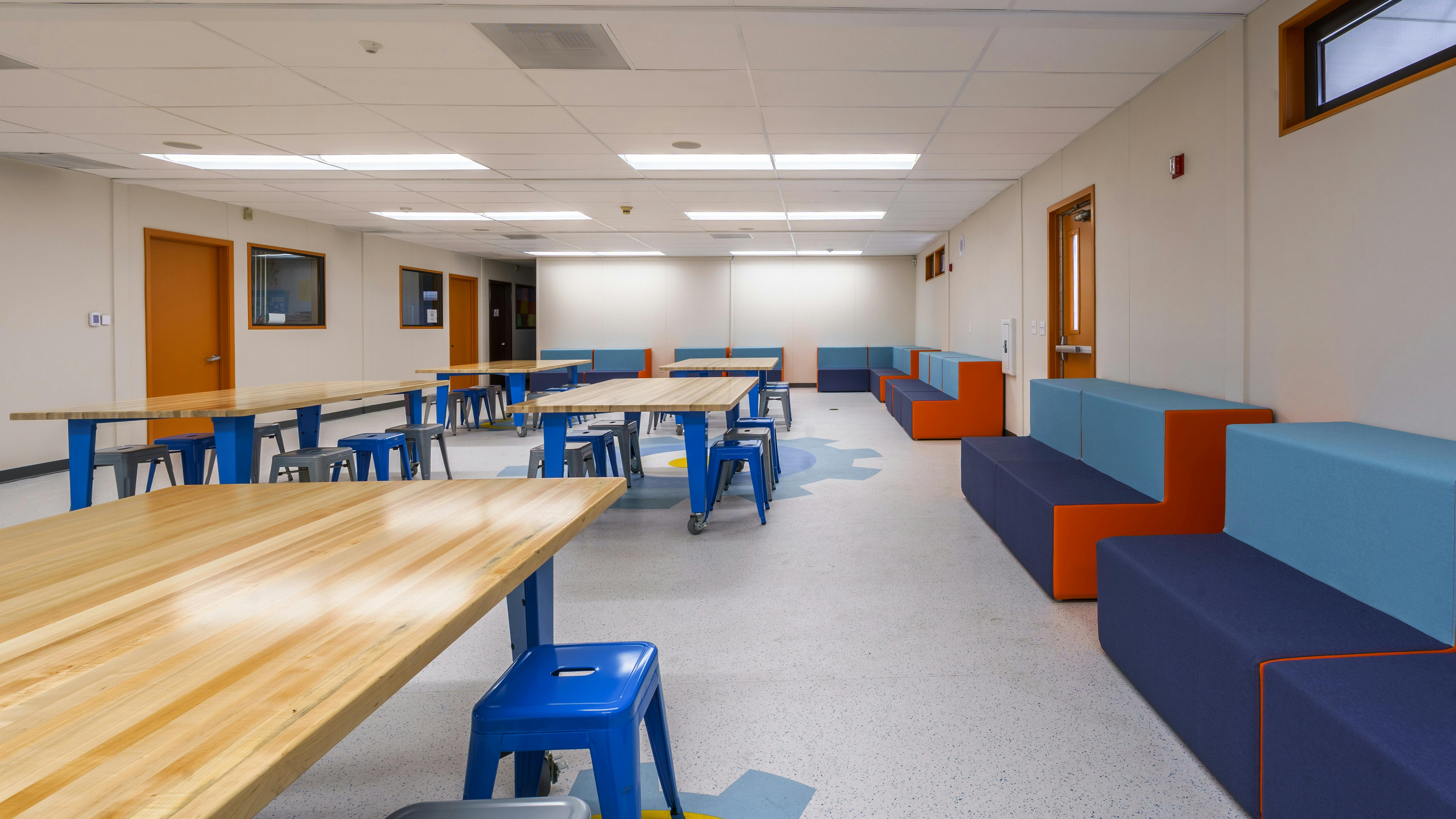 Open classroom space with movable wood-top tables and metal chairs with hard-surface flooring.