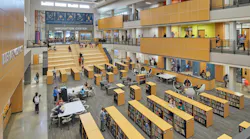 Large, open three-story learning commons with stadium seating/staircase and rows of bookshelves with seating and tables for study in between.
