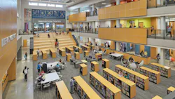 Large, open three-story learning commons with stadium seating/staircase and rows of bookshelves with seating and tables for study in between.