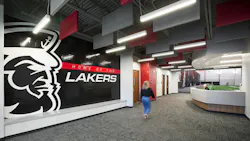 Woman walks toward reception area in hallway of new athletic faclity featuring large, branded graphic of school mascot and name with acoustic baffles and linear lighting fixtures above.