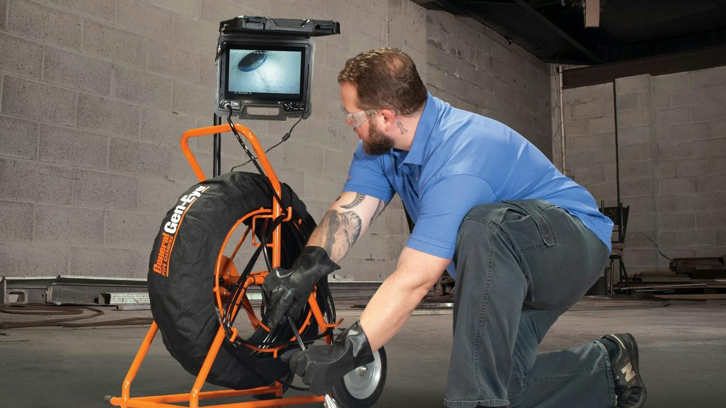 Maintenance technician uses pipe inspection cabling device while viewing attached monitor.