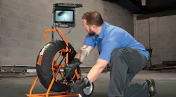 Maintenance technician uses pipe inspection cabling device while viewing attached monitor.