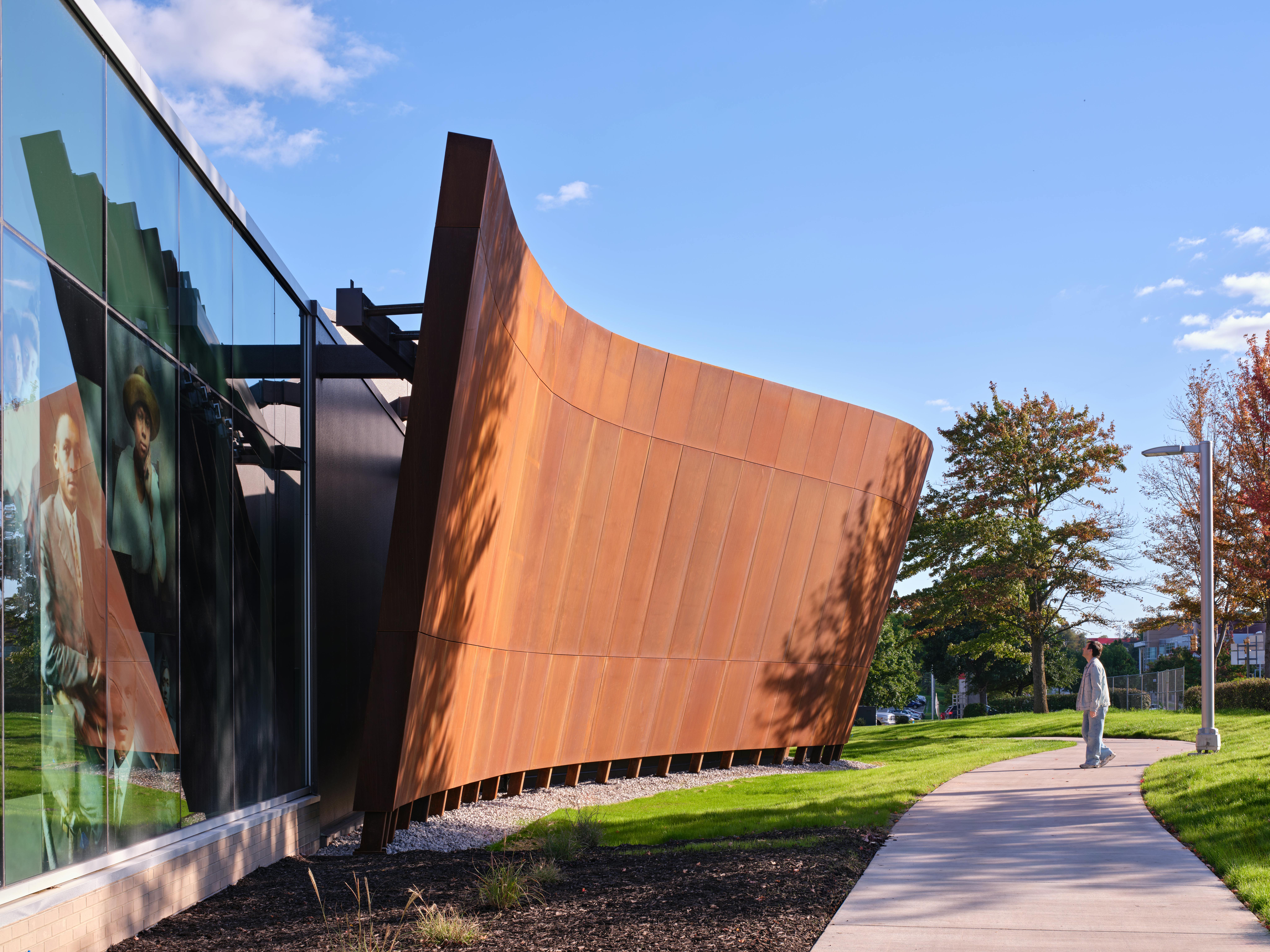 Curving, rusted-metal colored exterior of museum juxtaposed to glass facade.