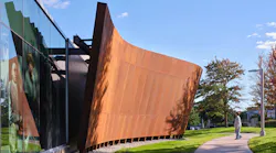 Curving, rusted-metal colored exterior of museum juxtaposed to glass facade.