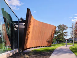 Curving, rusted-metal colored exterior of museum juxtaposed to glass facade.