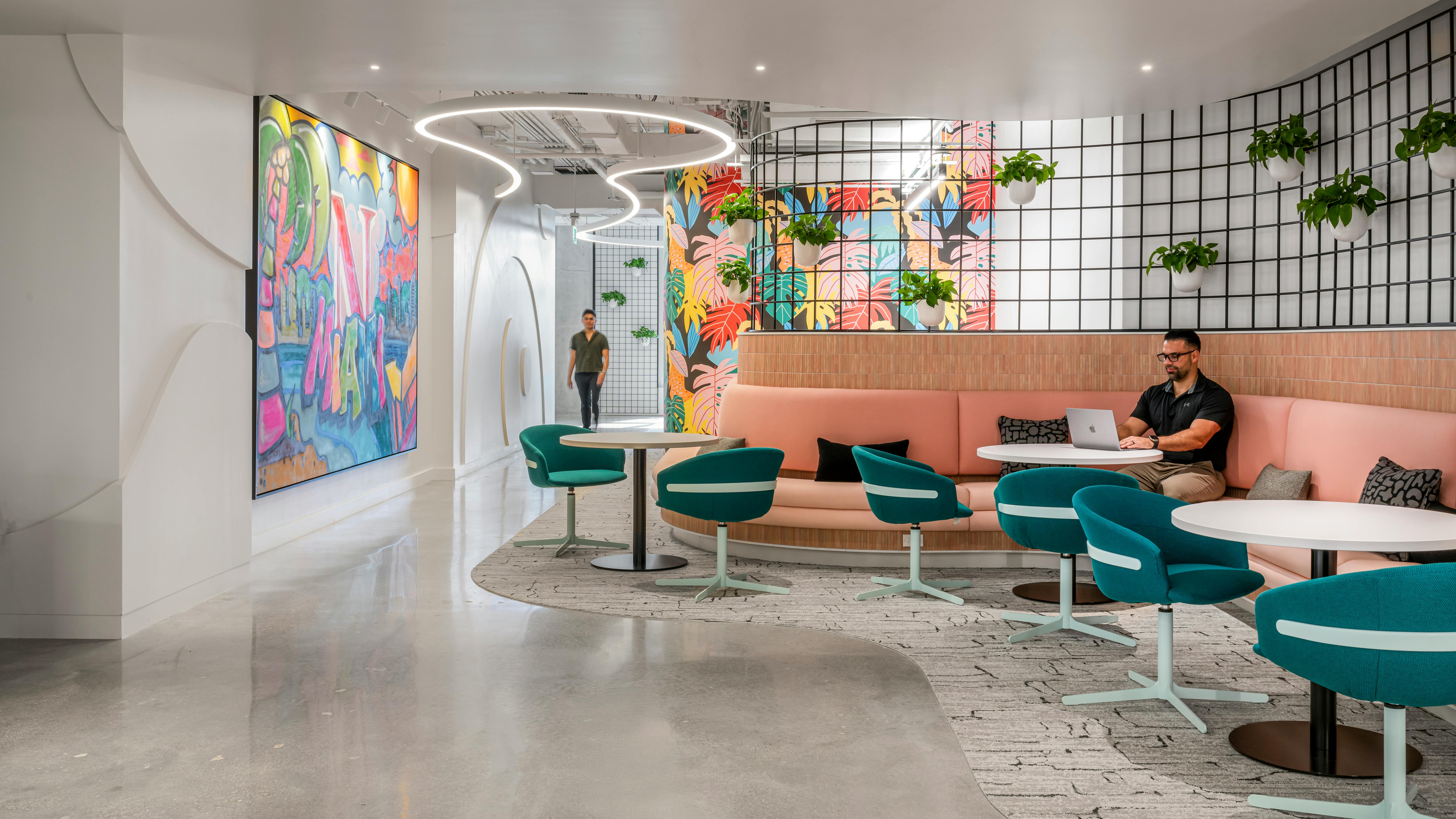 Student sits at curved bench seating area with tables surrounded by planters and colorful artwork.