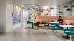 Student sits at curved bench seating area with tables surrounded by planters and colorful artwork.