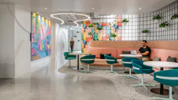 Student sits at curved bench seating area with tables surrounded by planters and colorful artwork.