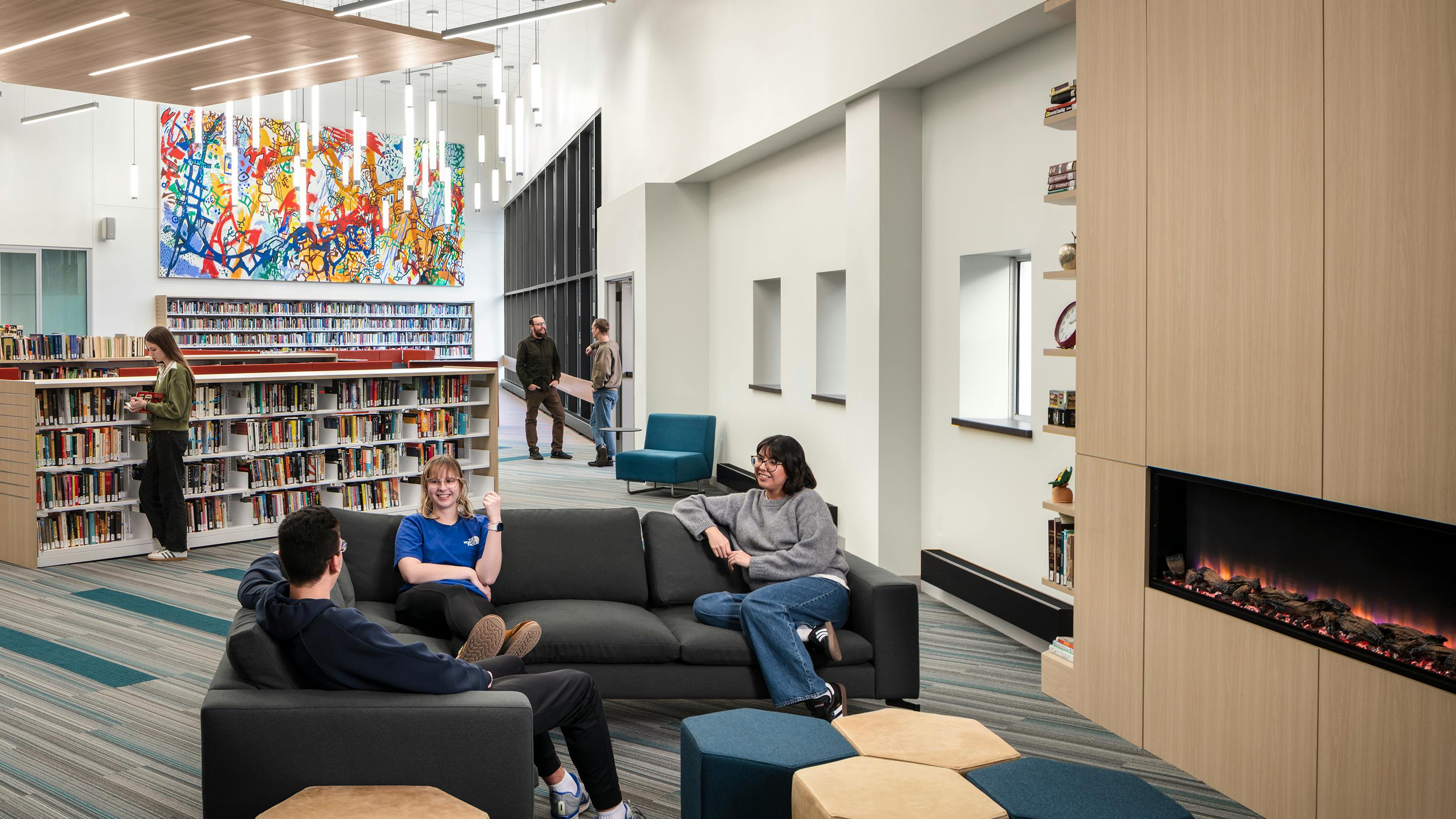 Students sit a lounge seating area next to fireplace with bookshelves in the background.