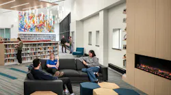Students sit a lounge seating area next to fireplace with bookshelves in the background.