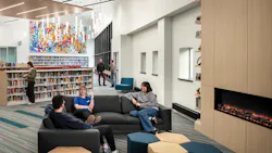 Students sit a lounge seating area next to fireplace with bookshelves in the background.
