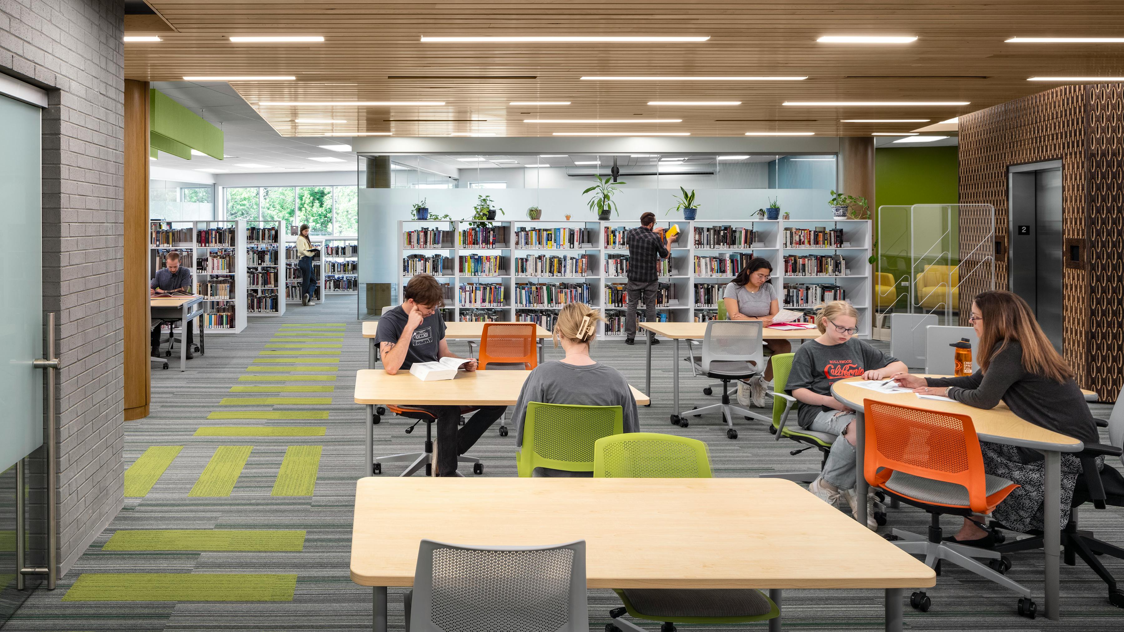 Students sit at tables studying in contemporary library with wood ceiling and linear lighting fixtures.
