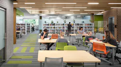 Students sit at tables studying in contemporary library with wood ceiling and linear lighting fixtures.