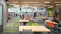 Students sit at tables studying in contemporary library with wood ceiling and linear lighting fixtures.