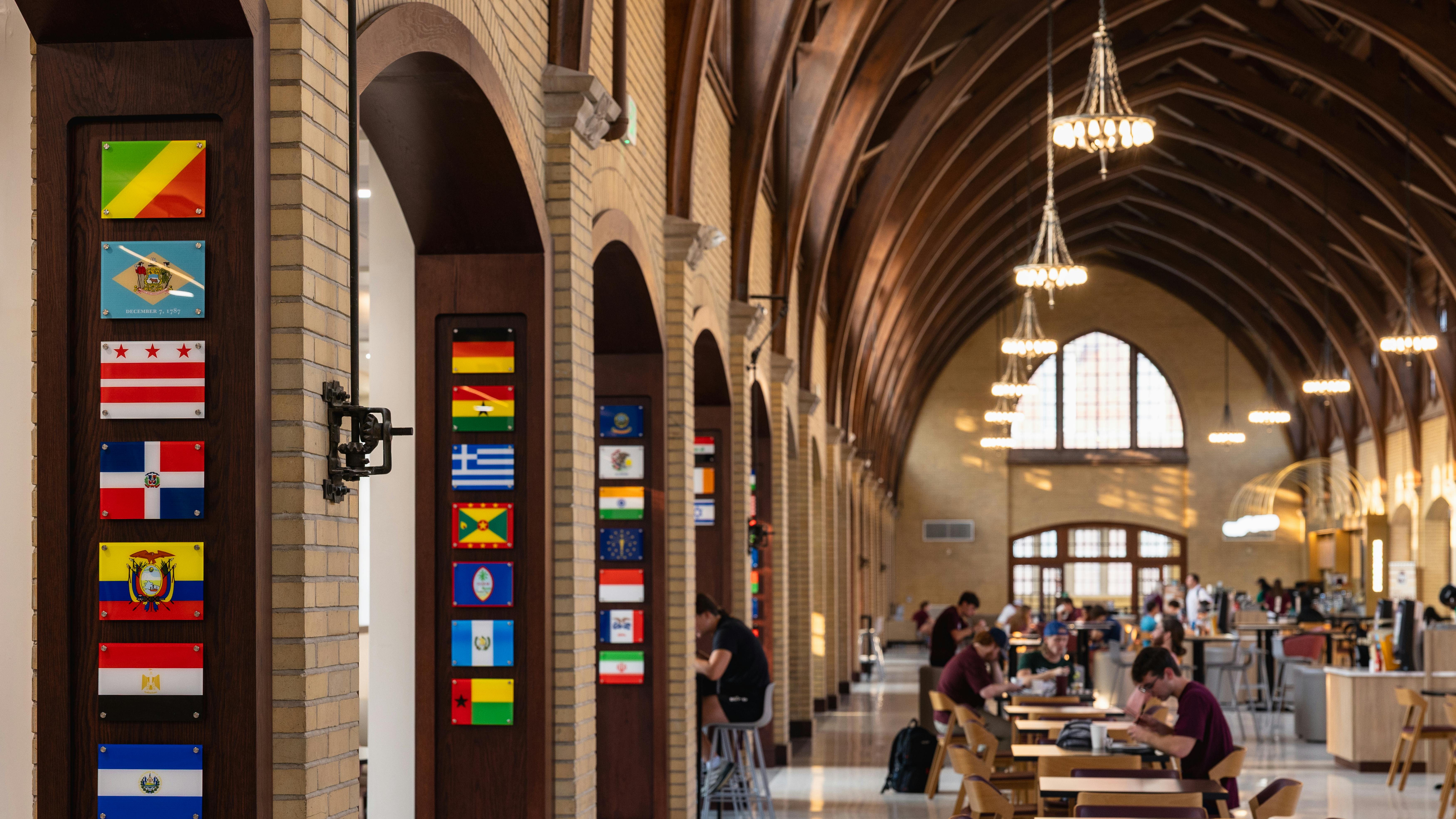 Newly renovated, historic dining hall with students sitting at tables beneath large, vaulted ceiling with curved wood beams.