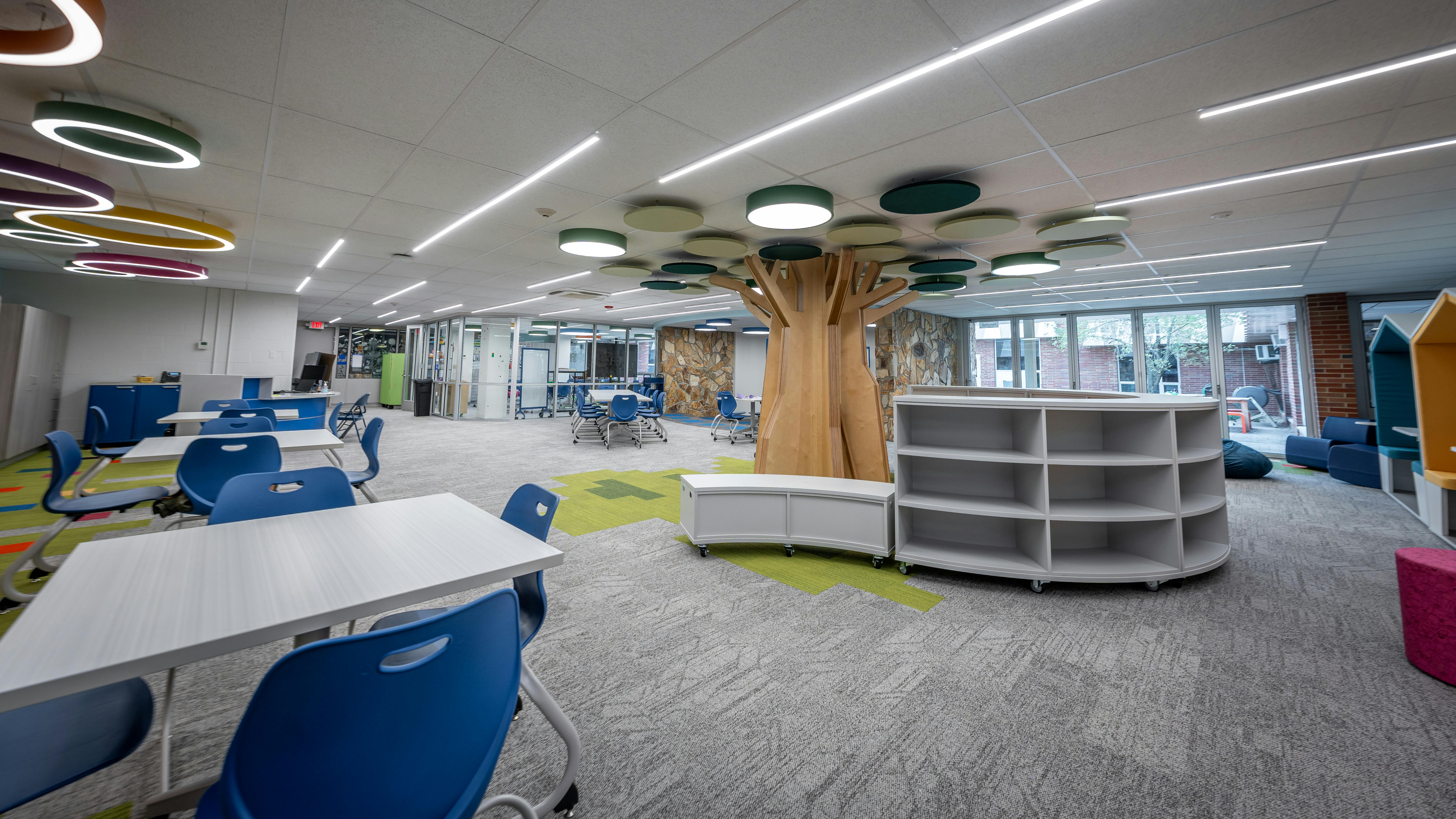 Media center with large, tree-like sculpture extending into ceiling with circular lighting and acoustic panels above and a variety of tables, seating, and storage below.