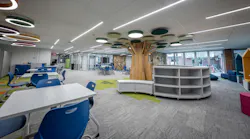 Media center with large, tree-like sculpture extending into ceiling with circular lighting and acoustic panels above and a variety of tables, seating, and storage below.