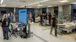 Nursing students move about a busy classroom simulation of a hospital wing.