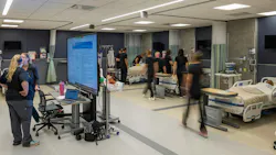 Nursing students move about a busy classroom simulation of a hospital wing.