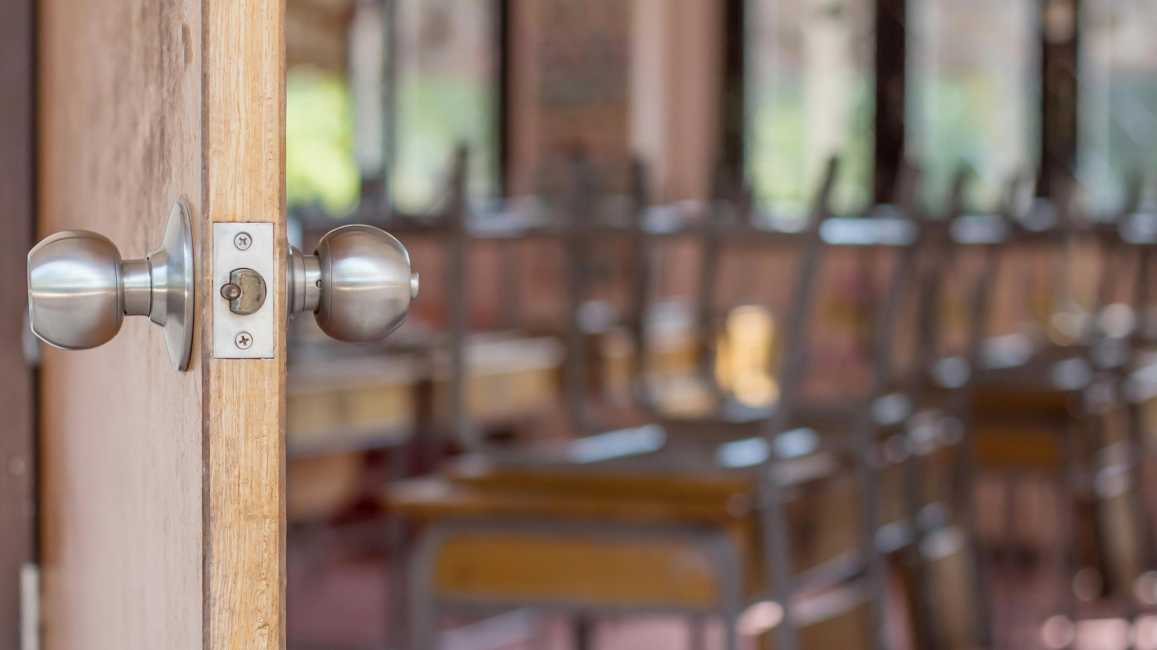 Close-up of door handle opening to empty classroom with chairs stacked upside-down on desks.