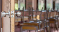 Close-up of door handle opening to empty classroom with chairs stacked upside-down on desks.