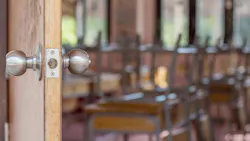 Close-up of door handle opening to empty classroom with chairs stacked upside-down on desks.