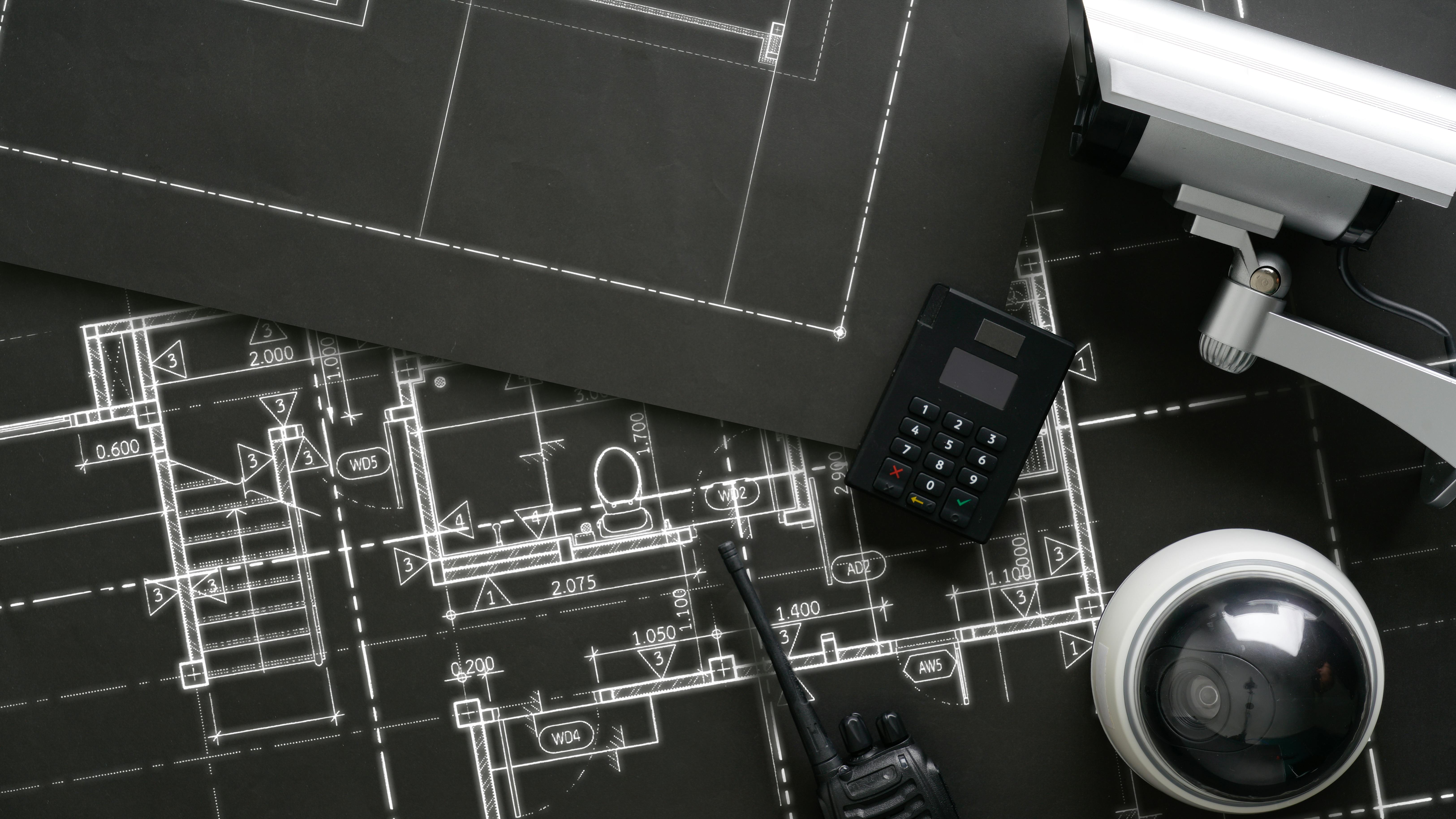 Building blueprints in black &amp; white with security camera and equipment sitting on top.