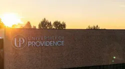 Exterior of campus building at sunset with University of Providence logo on side.