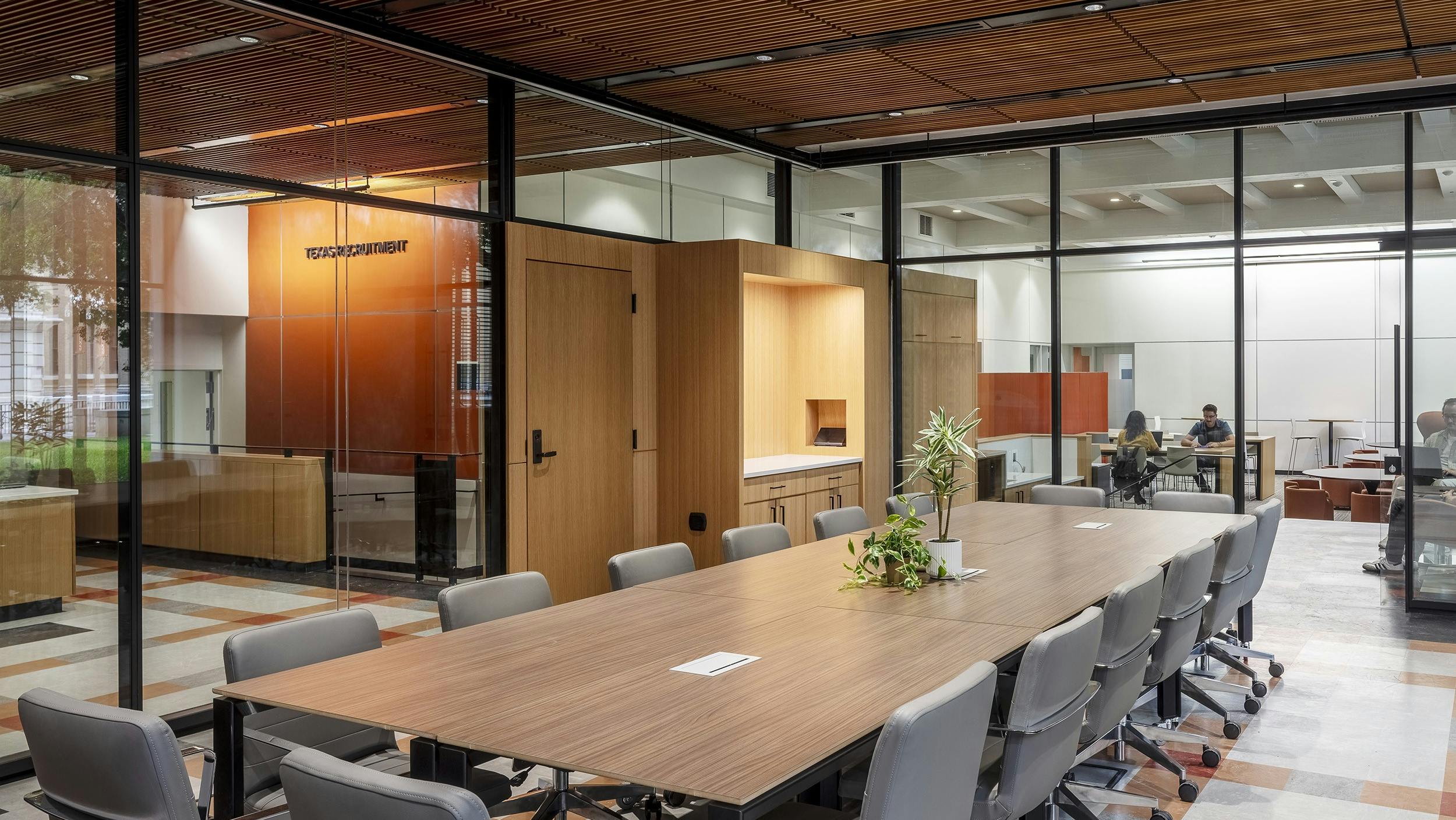 Modern, wood conference table and chairs with glass walls and offices in the background.