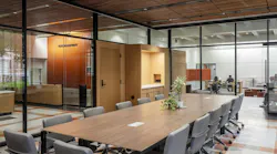 Modern, wood conference table and chairs with glass walls and offices in the background.