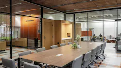 Modern, wood conference table and chairs with glass walls and offices in the background.